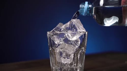 Close Up Transparent Clean Drinking Water Is Poured Into Glass with Cube Ice. The Glass Is Spinning