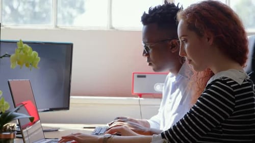 Side view of young mixed-race business team working on laptop and desktop pc in a modern office 4k