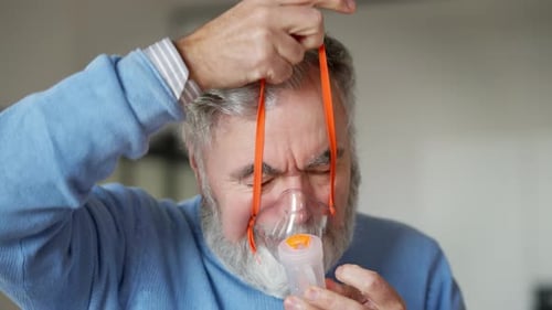 Gros plan d'un homme barbu âgé mettant un nébuliseur à l'intérieur