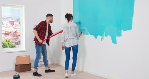 Kaukasisches glückliches junges Justmarried Paar malt Wände in blauer Farbe mit einer Wandwalze