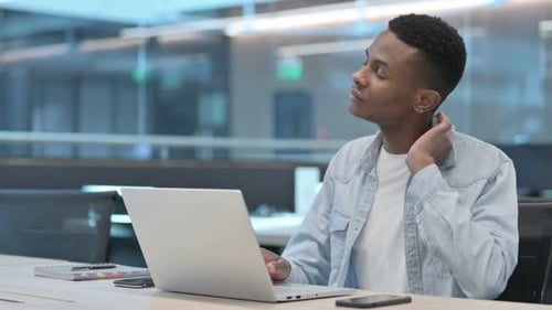 Young Man Rubs Neck While Typing at Computer