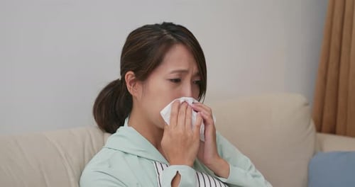 Woman Blowing Nose with Tissue on Couch