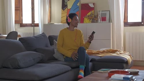 Frau mit Kopfhörern sitzt auf Sofa und hört Musik vom Smartphone