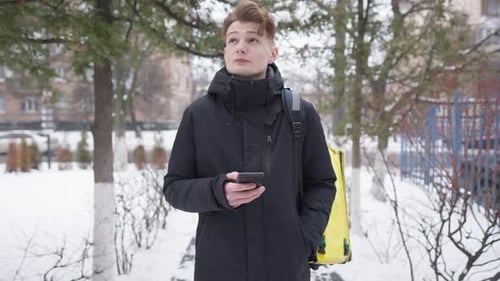 Young Adult Using Smartphone in Snowy Urban Park