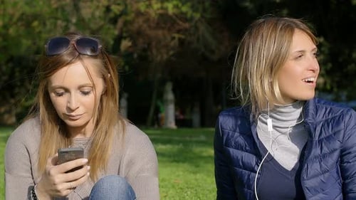 girlfriends in the park on the grass: having fun with smartphone and music
