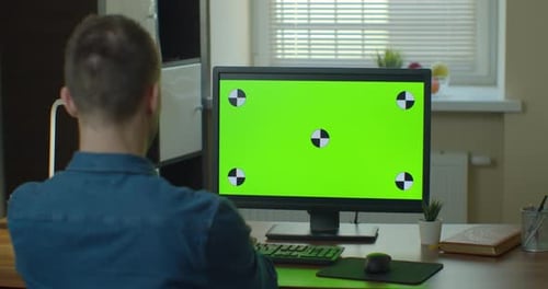Der Designer, der an seinem Schreibtisch sitzt, verwendet einen Desktop-Computer mit grünem Modellbildschirm.