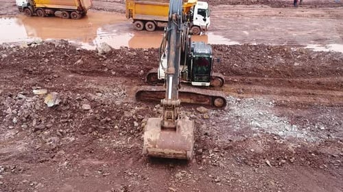 Excavator Digging in Muddy Construction Site Aerial View