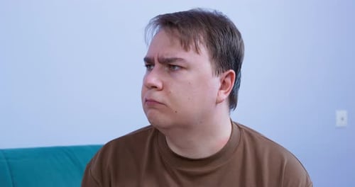 Confused Couple Sits on Sofa Looking at Each Other in Wonder