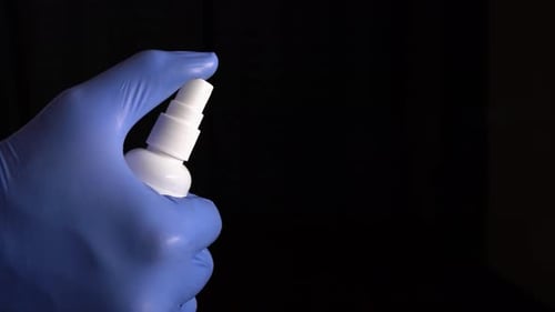 Gloved Hand Sprays Disinfectant from White Bottle