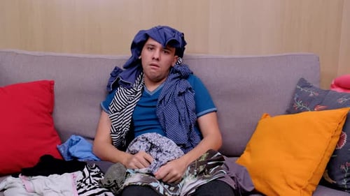 Young Adult Overwhelmed by Pile of Clothes on Couch
