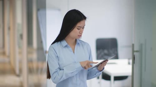Young Concentrated Asian Woman Manager Working on Digital Tablet Standing at Office Corridor Free