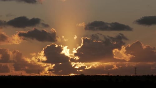 Statische Weitwinkelaufnahme gigantischer goldener Sonnenuntergangslichter, die hinter der Wolkensilhouette am Horizont leuchten.