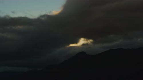 Himmel bei Sonnenuntergang bedeckt von dunklen Wolken mit Berg im Hintergrund