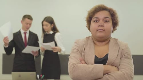 Portrait of Plump Woman in Formal Wear Looking in the Camera in the Foreground in the Office