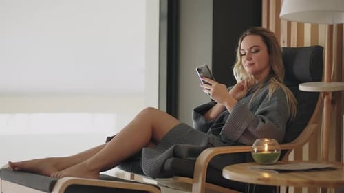 Relaxed Lady in Gown is Using Smartphone and Resting in Lounge Zone of Spa Center Portrait of Female