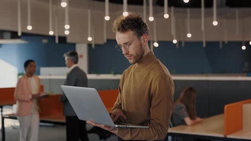 Successful Businessman in Formal Wear Standing at the Office with Laptop in Hands