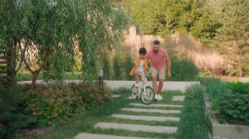 Father Teaching Son to Ride a Bicycle in Garden