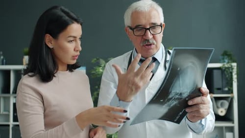 Patient and Doctor Looking at X-ray Image Talking Indoors in Office in Hospital