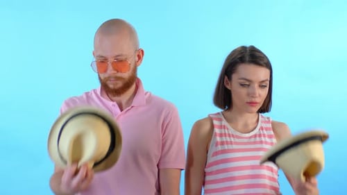 Couple Puts on Matching Hats on Light Blue Background