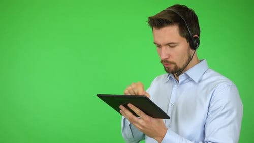 A Young Call Center Agent Works on a Tablet and Talks To a Caller, Then Smiles - Green Screen
