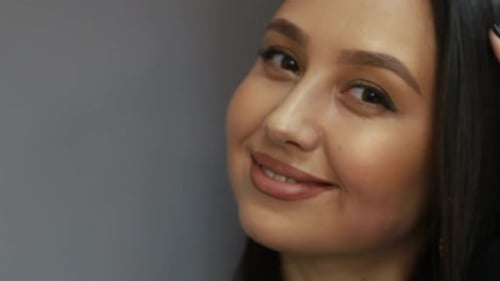 Brunette european woman looking at camera while standing in the office on gray background