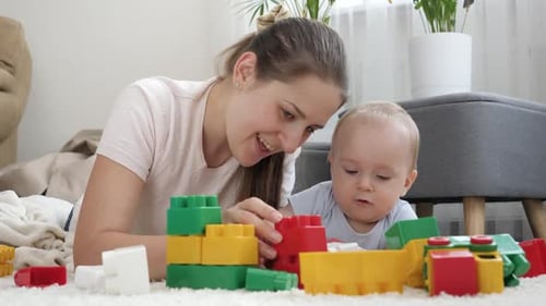 Happy Msiling Woman Playing with Her Baby Boy on Carpet and Building Toy Tower with Blocks and
