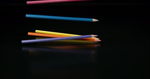 Colorful Pencils Falling onto Black Reflective Surface