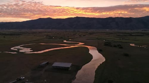 Rotating aerial view of pasture with winding river during colorful sunrise