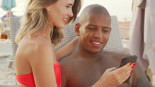Couple Relaxing on Beach Looking at Smartphone