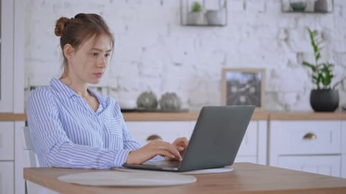 Woman Typing on Laptop at Kitchen Table