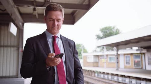 Businessman Checks Phone at Train Station Platform