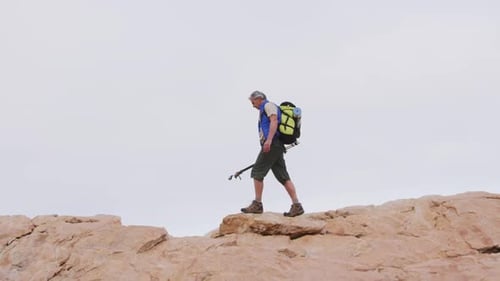 Senior Hiker Crosses Rocky Terrain with Backpack