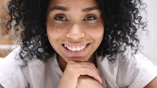 Close Up of Smiling AfroAmerican Woman Lying on Stomach in Bed Looking in Camera Laughing