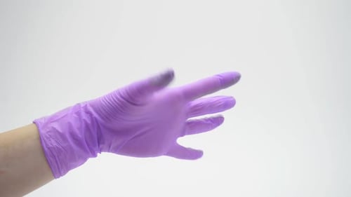 Main féminine en gros plan vêtue de latex, de nitrile, de caoutchouc, gant médical de couleur lilas sur un isolant