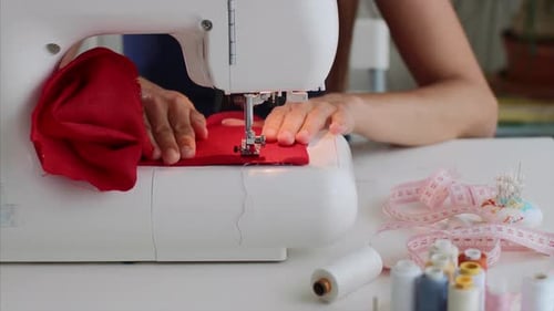 Couturière en gros plan, les mains d'une femme cousant un tissu rouge sur une machine à coudre sur le lieu de travail