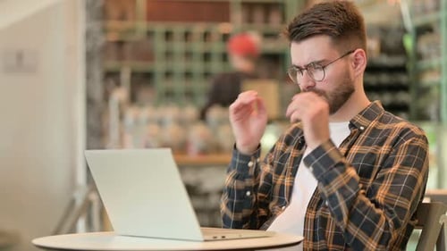 Young Man with Laptop Having Headache in Cafe