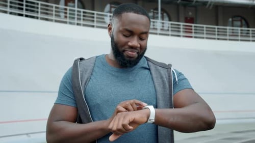 Man Reading Good News on Smartwatch at Stadium. Guy Using Smartwatch Outdoors