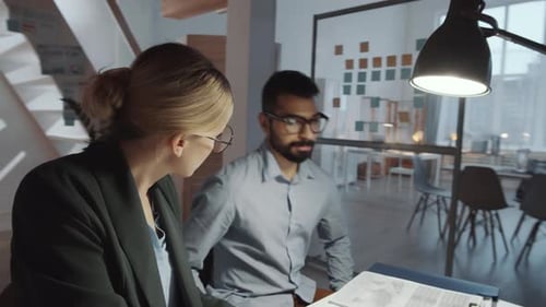 Male and Female Coworkers Discussing Business Documents at Office Desk