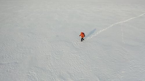 View From Drone a Lone Traveler with a Backpack Walks Through the Snowy Desert