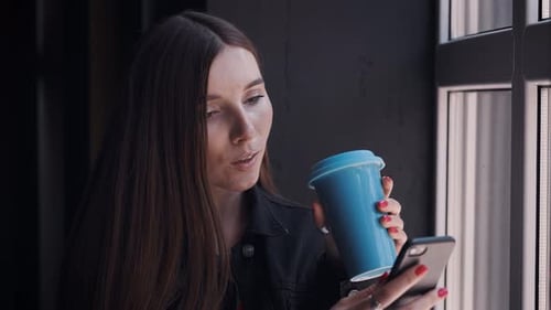 Woman Using Phone and Drinking Coffee Indoors