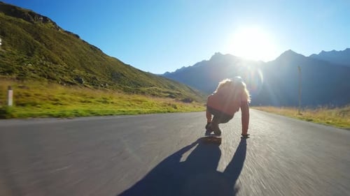 Person Longboarding Down Mountain Road on Sunny Day