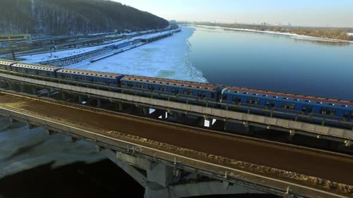 Luftaufnahme U-Bahn fährt auf Brückenbahn über winterliche Flusslandschaft