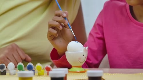 Cute Little Girl with Funny Bunny Ears Decorates Eggs with Brush and Paints
