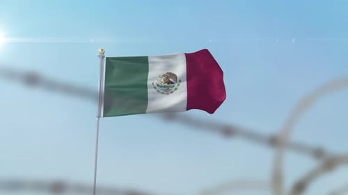 Mexican Flag Waving Behind Barbed Wire Against Blue Sky
