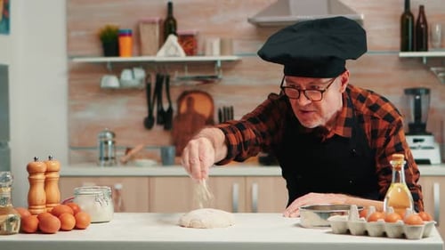 Baker sprinkling flour on dough in kitchen