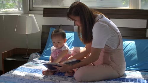 Mother Reads Book to Baby on Bed