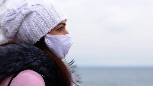 A woman with long dark hair in a mask from air pollution and the Covid19 coronavirus walk