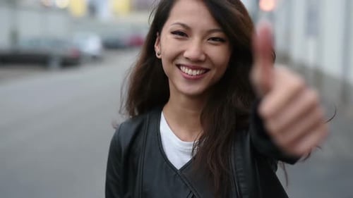 Young asian woman smiling with thumb up outdoor in the city, looking at camera