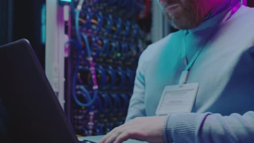 Adult Works Laptop In Server Room At Night