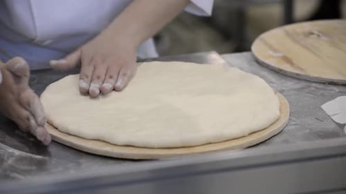 Person Stretching Pizza Dough in Commercial Kitchen